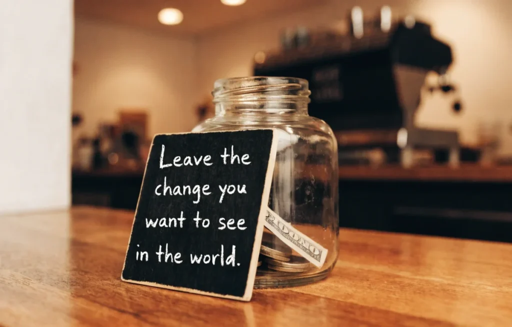 Funny tip jar on a coffee shop counter with a handwritten pun sign to encourage customer tipping
