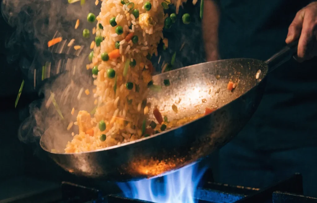 Sizzling fried rice in a hot wok with vegetables and egg being tossed over a flame — illustrating fried rice puns section
